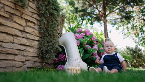 cute baby boy celebrating his first birthday. lovely child sits on the grass in the garden with a cake and balloon shaped like number one.