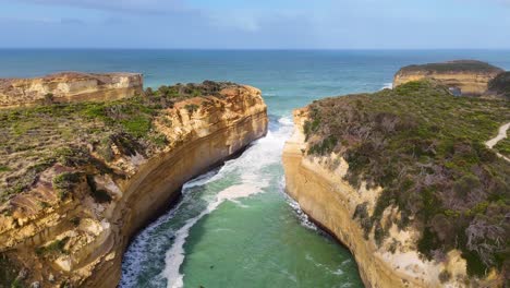 drone footage captures the rugged cliffs and turquoise waters of loch ard gorge, port campbell, under clear skies
