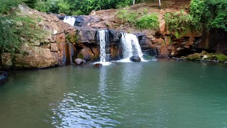 Vista-Aérea-De-Una-Exuberante-Laguna-Verde-Con-Una-Pequeña-Cascada-De-Aguas-Cristalinas