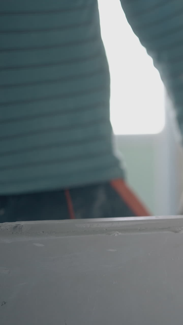 professional repair worker in gloves holds grey gypsum plasterboard construction and beats with rubber hammer closeup