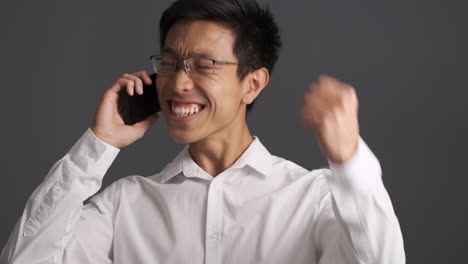 Asian-man-calling-on-smartphone-and-celebrating.