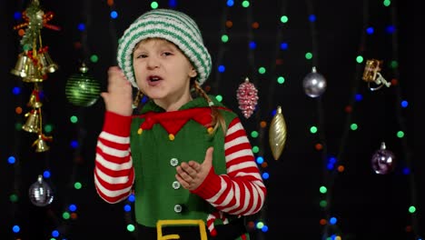 Kid-girl-in-Christmas-elf-Santa-Claus-helper-costume-blows-air-kiss-isolated-on-black-background