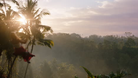 happy woman swinging over jungle at sunrise travel girl enjoying exotic vacation on swing with sun flare shining through palm trees in tropical rainforest holiday lifestyle freedom