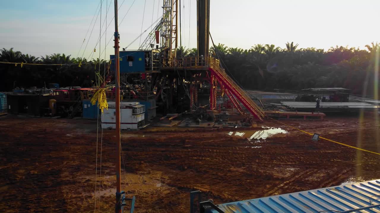 imágenes cinematográficas de drones de 4k de la estructura del equipo de la plataforma de perforación en tierra para la exploración y explotación de petróleo en medio de la jungla rodeada de palmeras durante la puesta de sol y el alto precio del petróleo