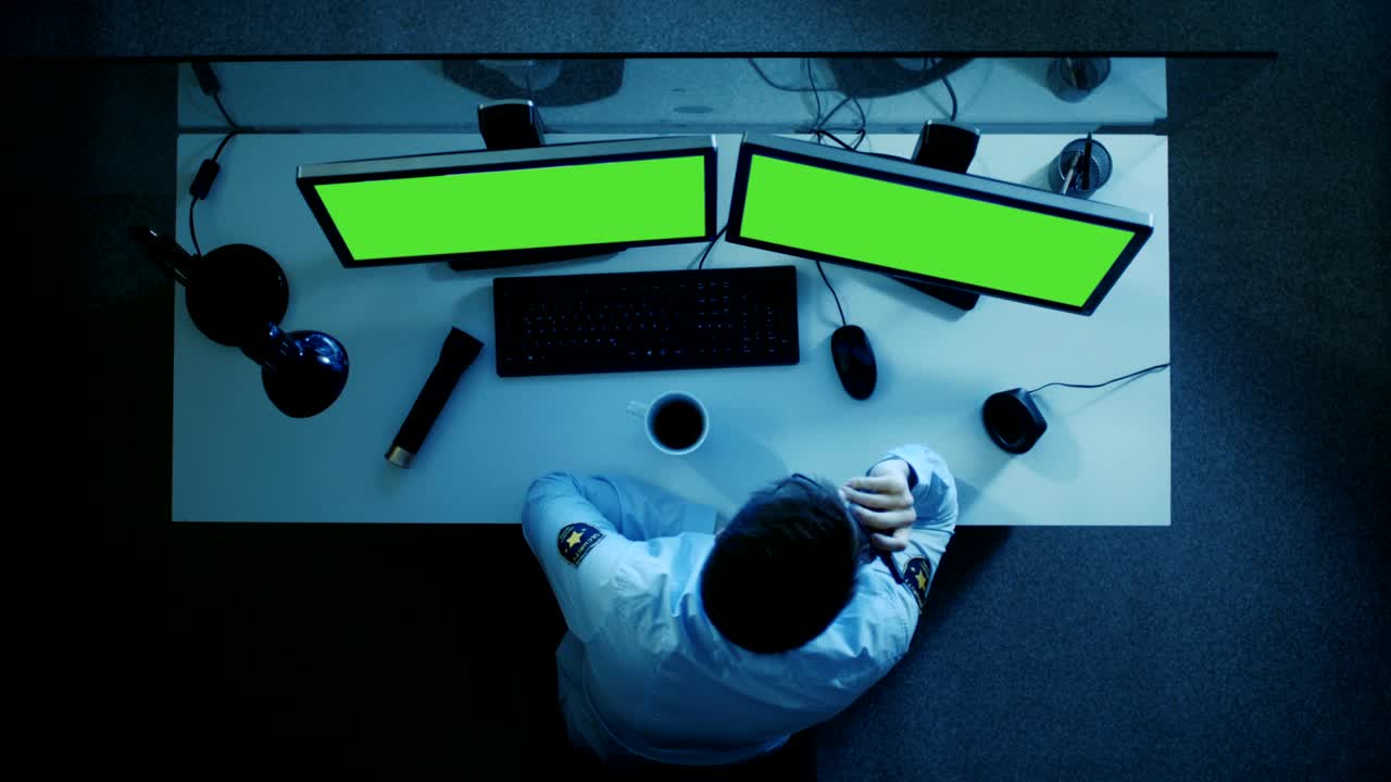 Top View of a Security Guard Looking at Green Screen Monitors and Talking on Walkie Talkie. He's Working Night Shift.