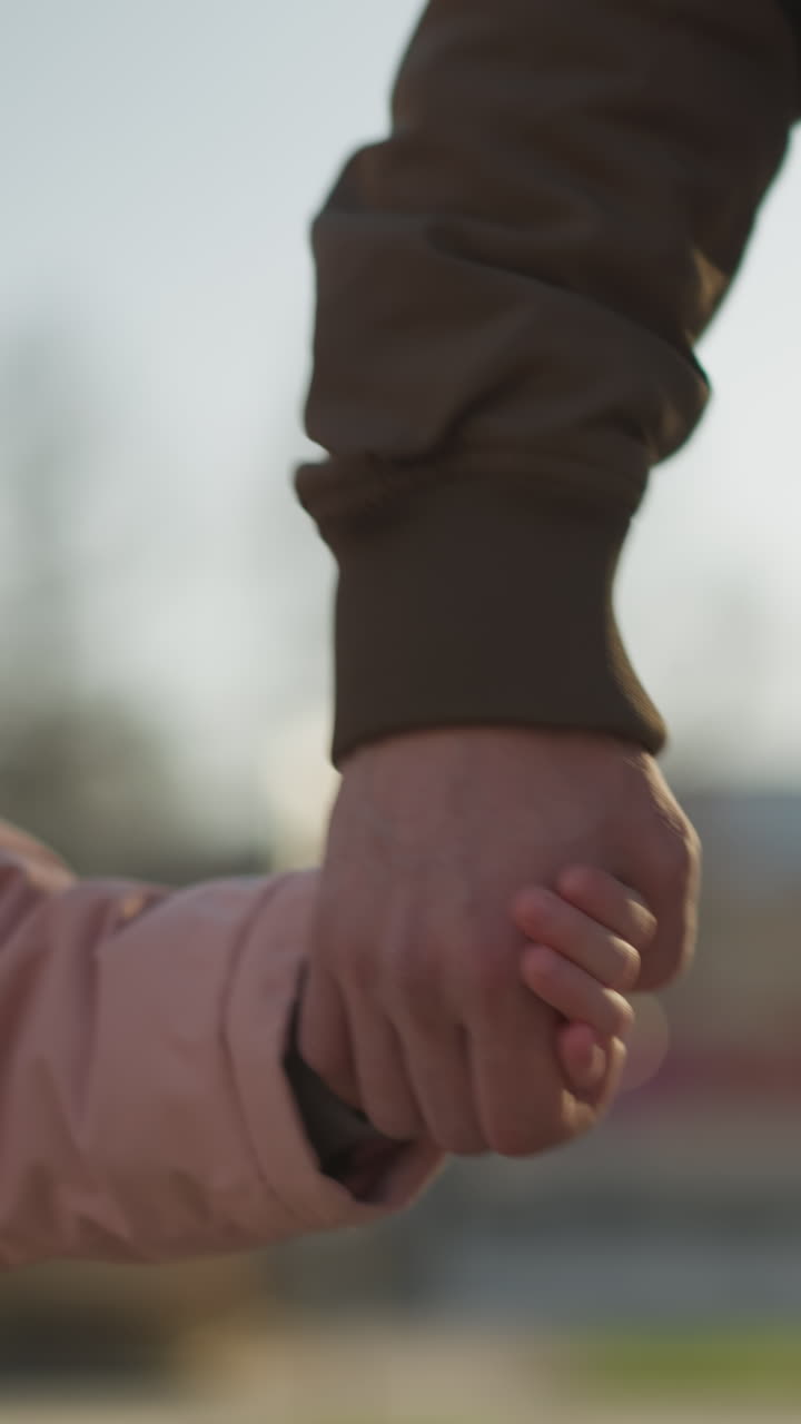 vista frontal de una niña pequeña con una chaqueta rosada tomándose de la mano con un hombre sin rostro con una jaqueta marrón y pantalones vaqueros azules. la escena captura un momento de conexión y calor en un día soleado