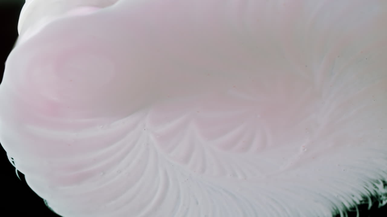 Crema blanca abstracta extendiéndose y arremolinándose sobre una superficie negra