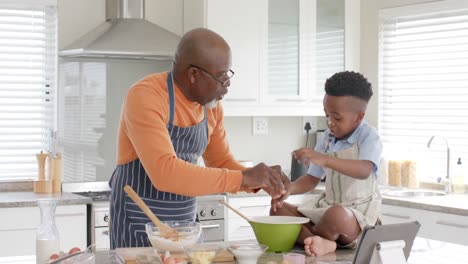 Happy-african-american-grandfather-and-grandson-high-fiving,-baking-in-kitchen,-slow-motion