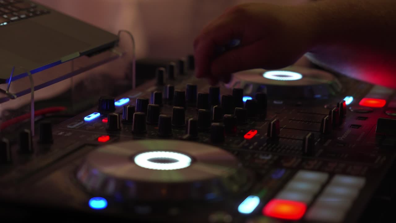 Vista ravvicinata di un DJ di matrimonio che regola i controlli del mixer durante una celebrazione di ricevimento con illuminazione colorata da festa.
