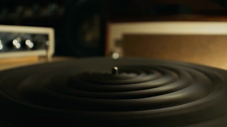 Una prospettiva ravvicinata al piatto mostra un disco in vinile nero che poggia sul perno metallico sopra la superficie scanalata del giradischi, con sfocatura morbida, ombre calde, riflessi circolari e un'atmosfera d'ascolto nostalgica