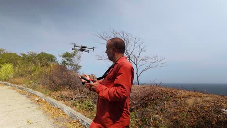 latin man lands drone on hands and holds controller with a screen on coastal road with sea background.