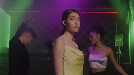 portrait of beautiful girl looking confident at camera at disco while her friends dancing behind her 1