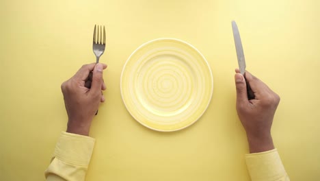 mano sosteniendo cubiertos con un plato vacío en una mesa de madera