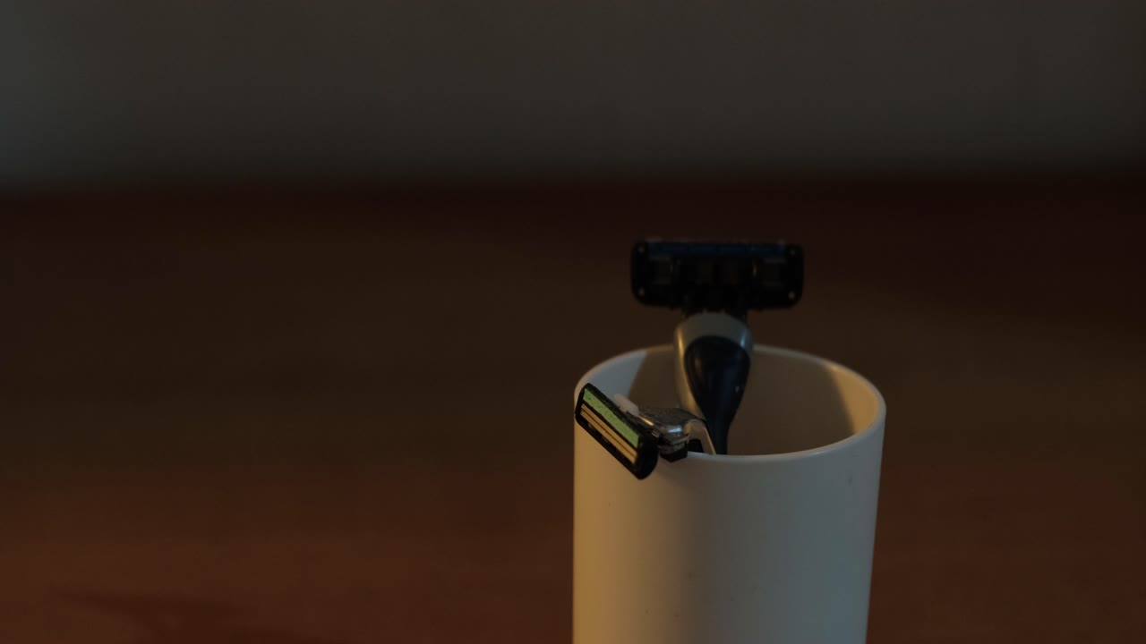 Hand placing manual razor in a cup with other safety razors indoors - static medium shot