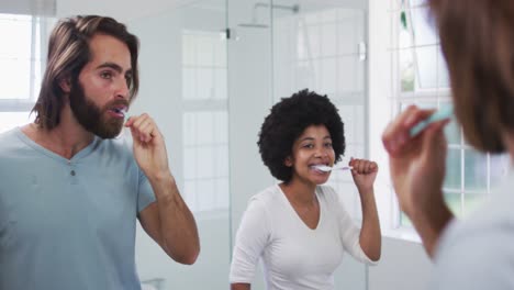 pareja de raza mixta cepillando juntos mientras miraban en el espejo en el baño