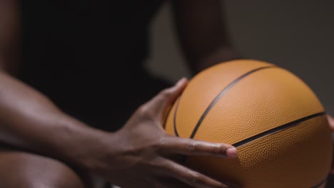 Nahaufnahme-Eines-Sitzenden-Männlichen-Basketballspielers-Mit-Händen,-Die-Den-Ball-Halten