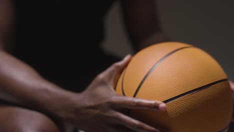 close up studio shot of seated male basketball player with hands holding ball