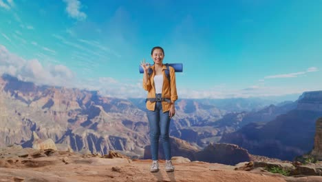 full body of asian female hiker with mountaineering backpack smiling and showing okay gesture to camera while traveling at the top of mountain