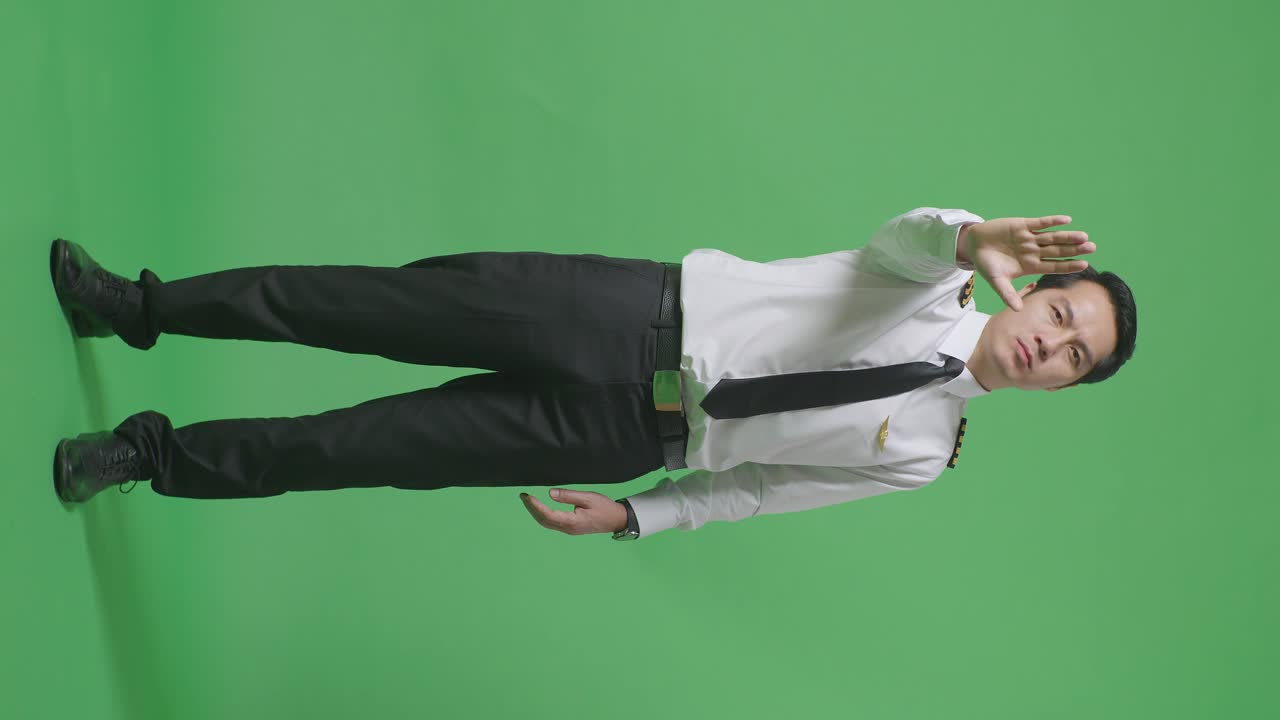 아시아 남성 조종사가 카메라를 바라보고 녹색 스크린 배경 스튜디오에서 손 표시 없이 불쾌감을 표합니다.