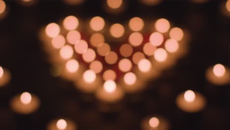 Defocused-Shot-Of-Romantic-Red-And-White-Candles-In-the-Shape-Of-A-Heart-On-Black-Background