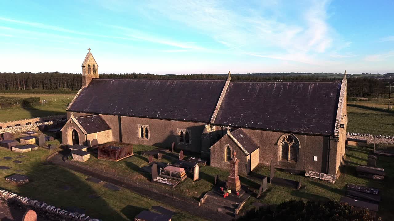 St Peters church in rural Newborough aerial orbit view across Welsh slate gravestones at sunrise
