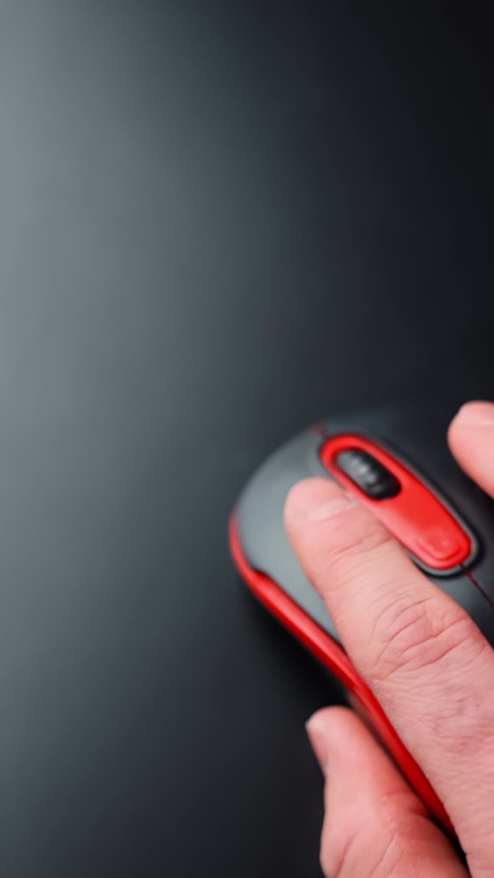 Vertical close-up of a hand using a red and black computer mouse on a dark desk with copy space. Soft blur motion, calm focused work vibe