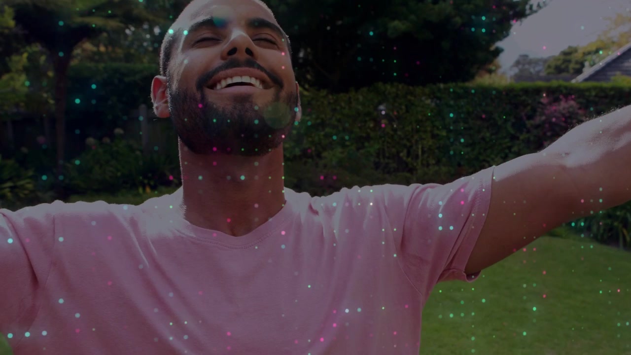 Shot panning up, man in pink tee raising face, arms in garden, sparkles surrounding for lifestyle