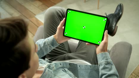 vista desde el hombro del hombre sosteniendo y usando gestos de la mano en la pantalla de maqueta verde computadora tableta digital sentada en una silla. hombre comprando cosas o navegando. tocando en la pantalla central