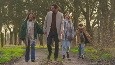 Full-length-shot-of-family-holding-hands-on-walk-through-autumn-countryside-together---shot-in-slow-motion