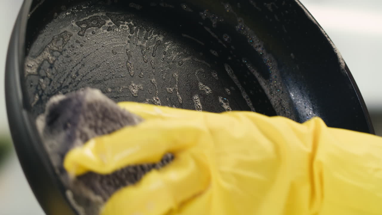 Hand in Yellow Glove Cleaning Frying Pan with Sponge
