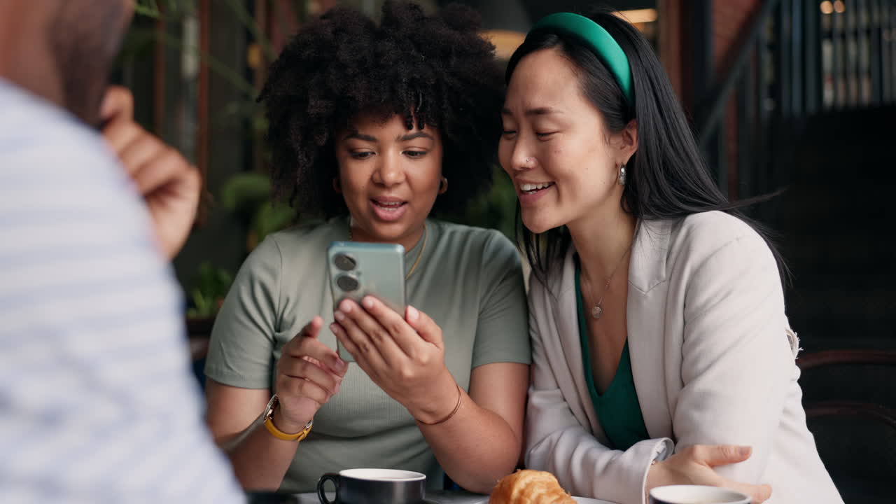 Two friends laughing at a phone in a cafe