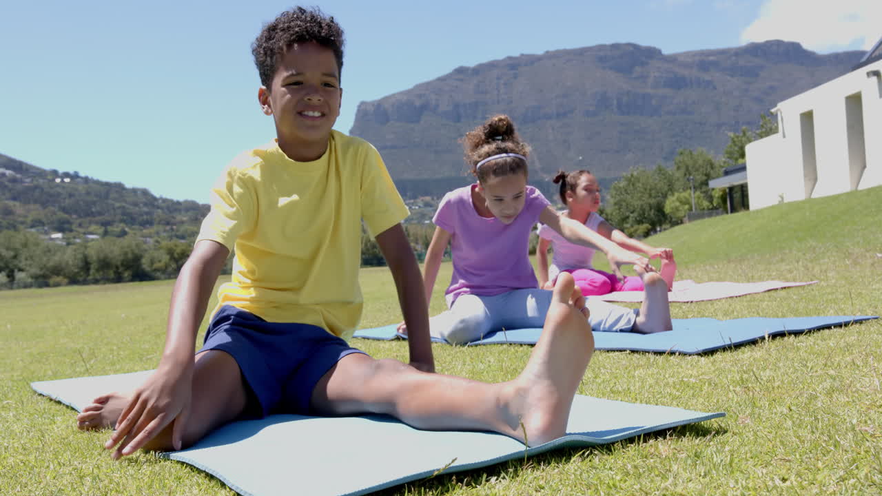 Biracial boy and girls practice yoga outdoors, with mountains in the background, in school