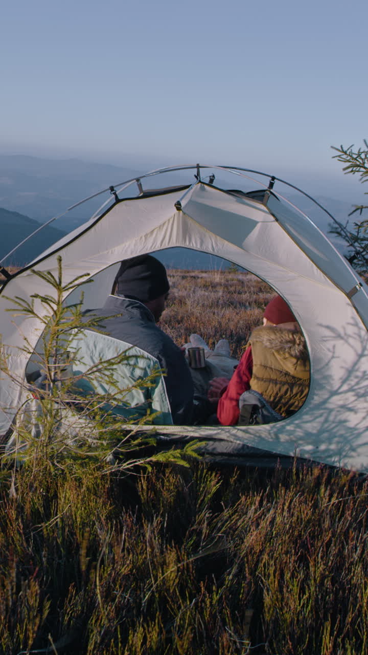 다민족 관광 부부는 산꼭대기에 텐트에 앉아 대화를 나누고 차를 마시며 모험 휴가 중에 휴식을 취하기 위해 멈습니다. 만적 인 하이커 가족은 풍경을 감상합니다. 수직