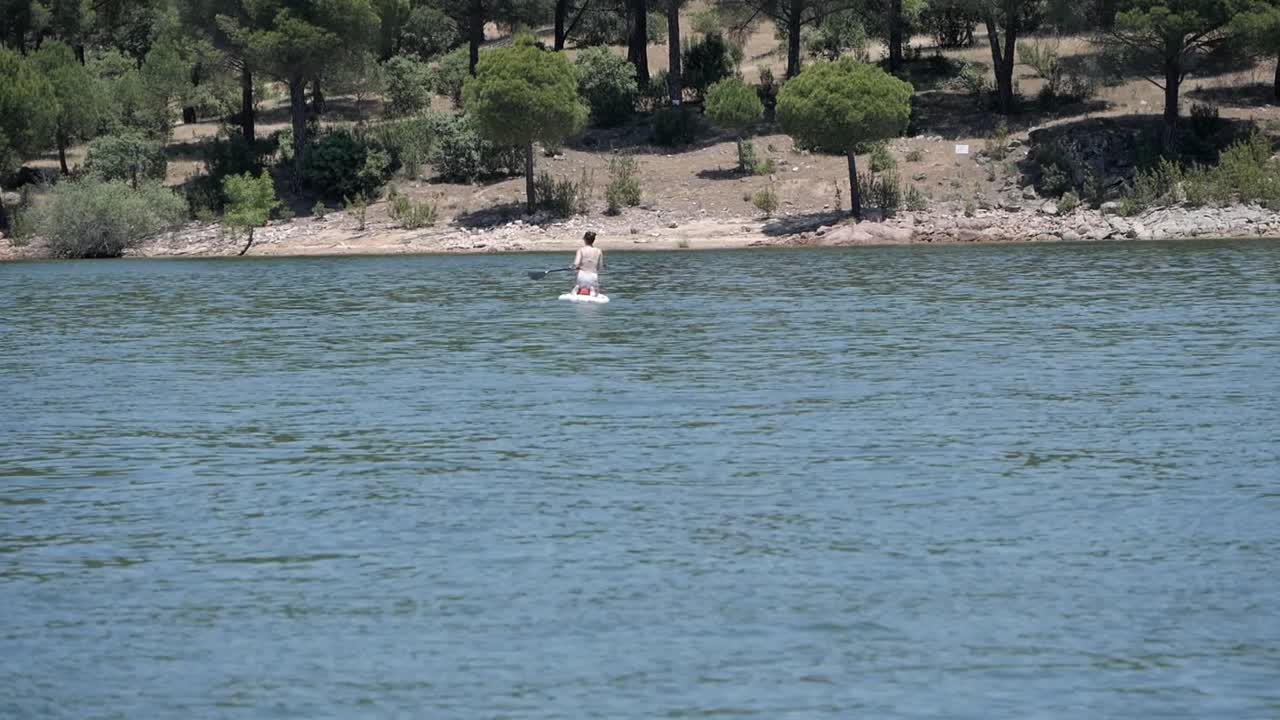 mujer de rodillas remando encima de stand up paddle board en el lago, pantano de san juan, madrid