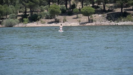 mujer de rodillas remando encima de stand up paddle board en el lago, pantano de san juan, madrid