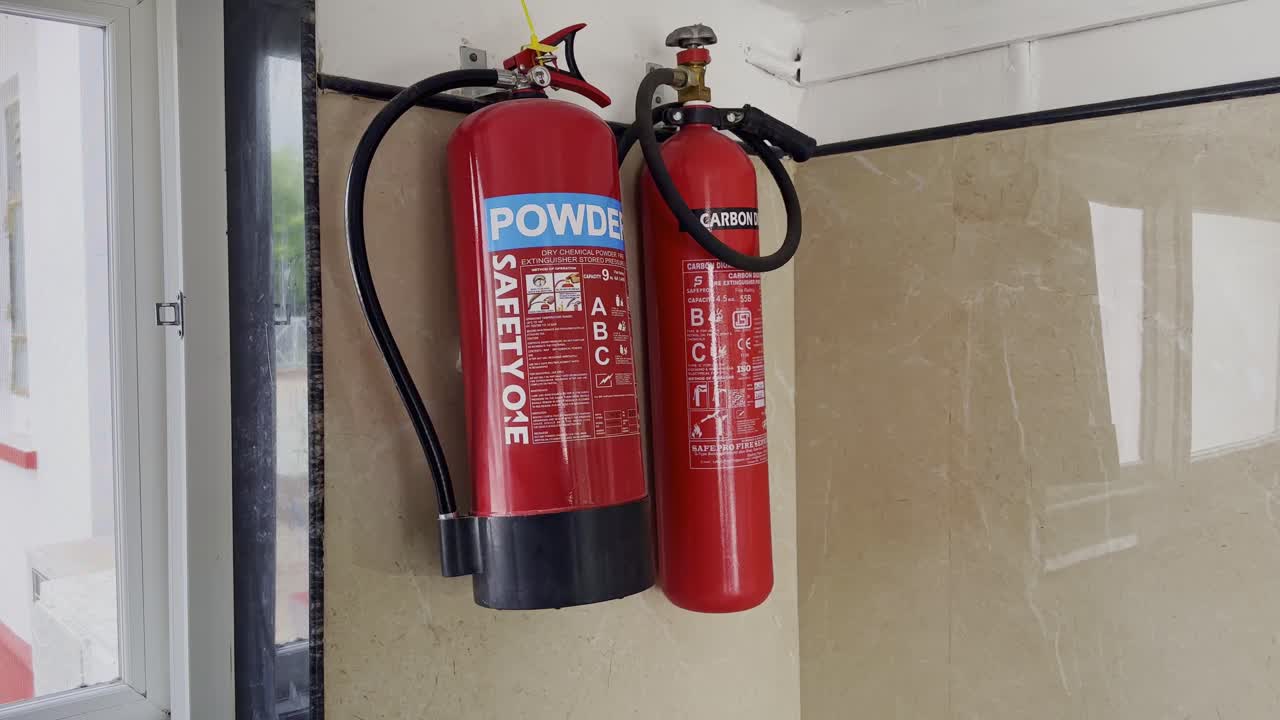 Close-up of powder and carbon dioxide fire extinguishers hanging on a wall indoors, essential safety equipment for emergencies