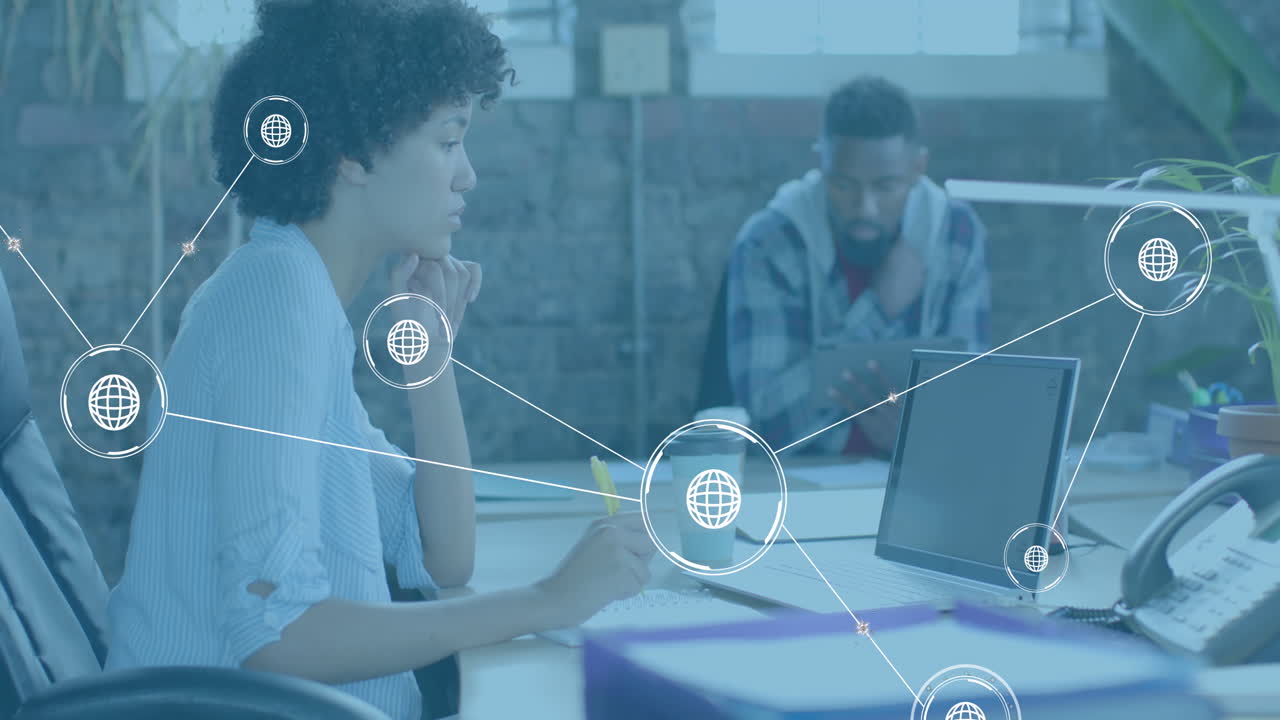 Animation of globe icons over diverse business people using laptop in office