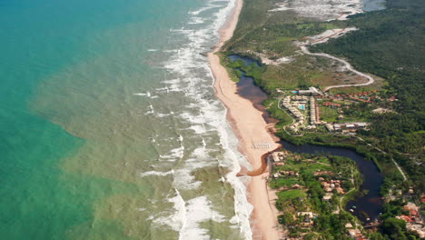 Aerial-view-of-the-waves,-beach,-a-small-river-and-the-palm-trees-area-in-a-cloudy-day,-Imbassai,-Bahia,-Brazil