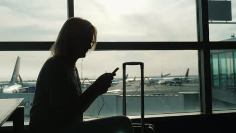 woman with suitcase uses phone in airport