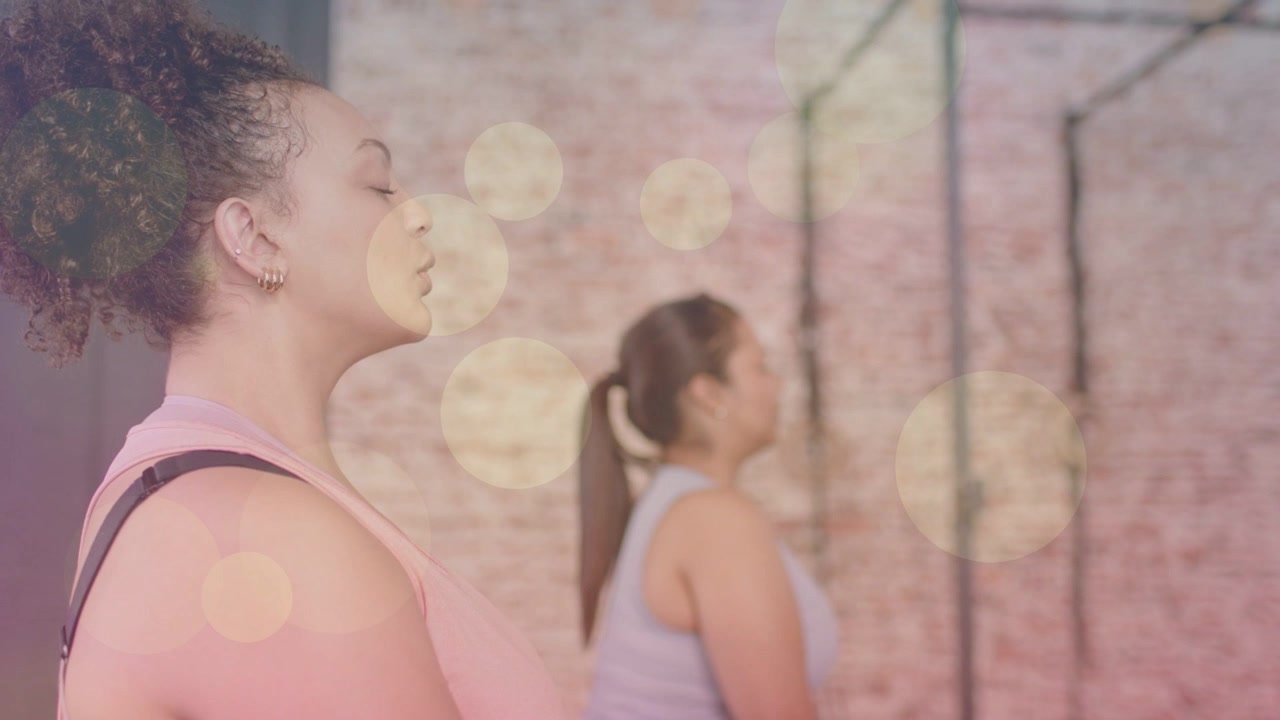 Dos mujeres meditando en un entorno de fitness, respirando para la calma mientras el efecto bokeh se intensifica a su alrededor.