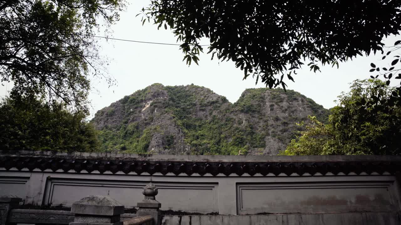 A tranquil, fixed shot of the lush limestone mountains captured from the grounds of Thai Vi Temple in Tam Coc, Vietnam. karst formations surrounded by greenery of Vietnam's natural beauty