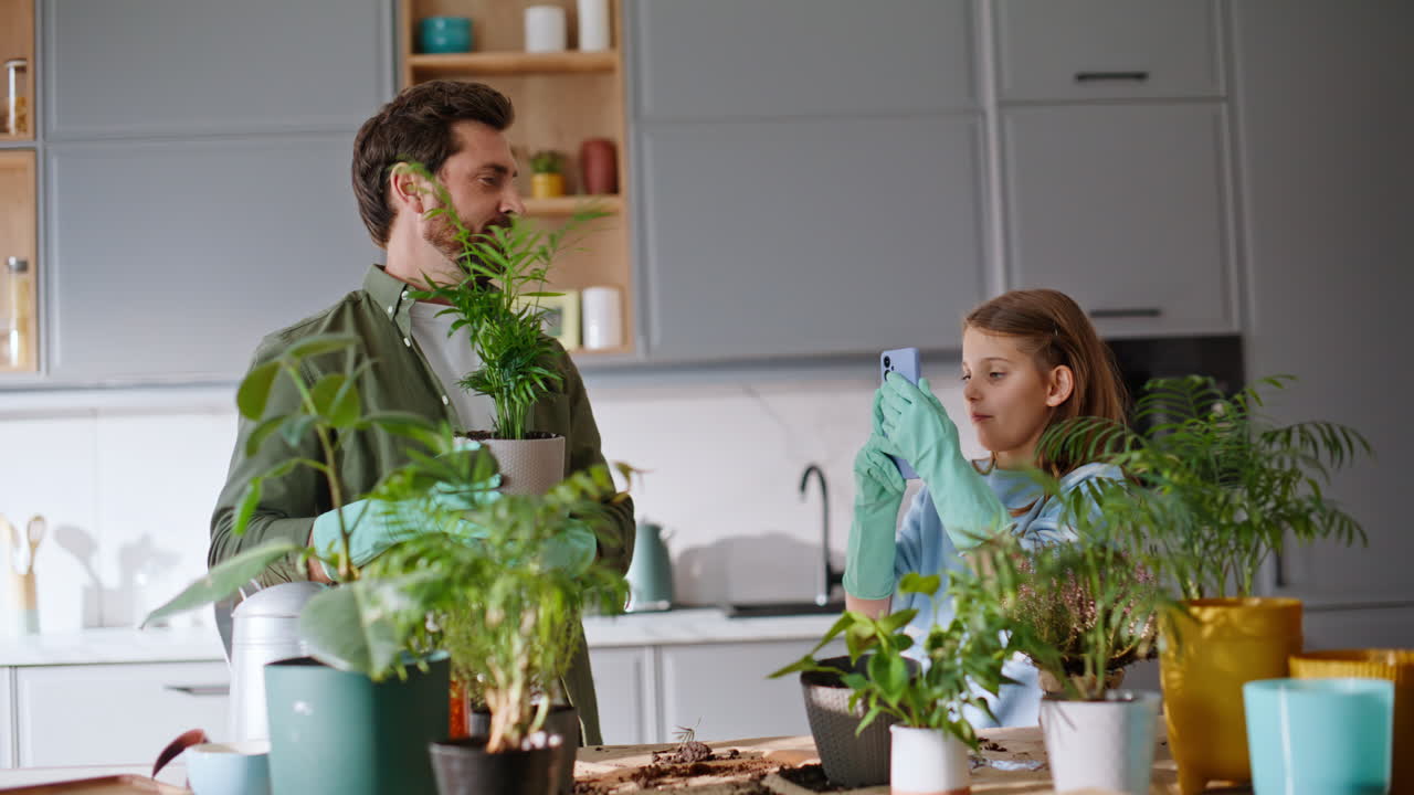Figlia che riprende il padre mentre fa giardinaggio con il cellulare a casa, primo piano del tempo libero in famiglia