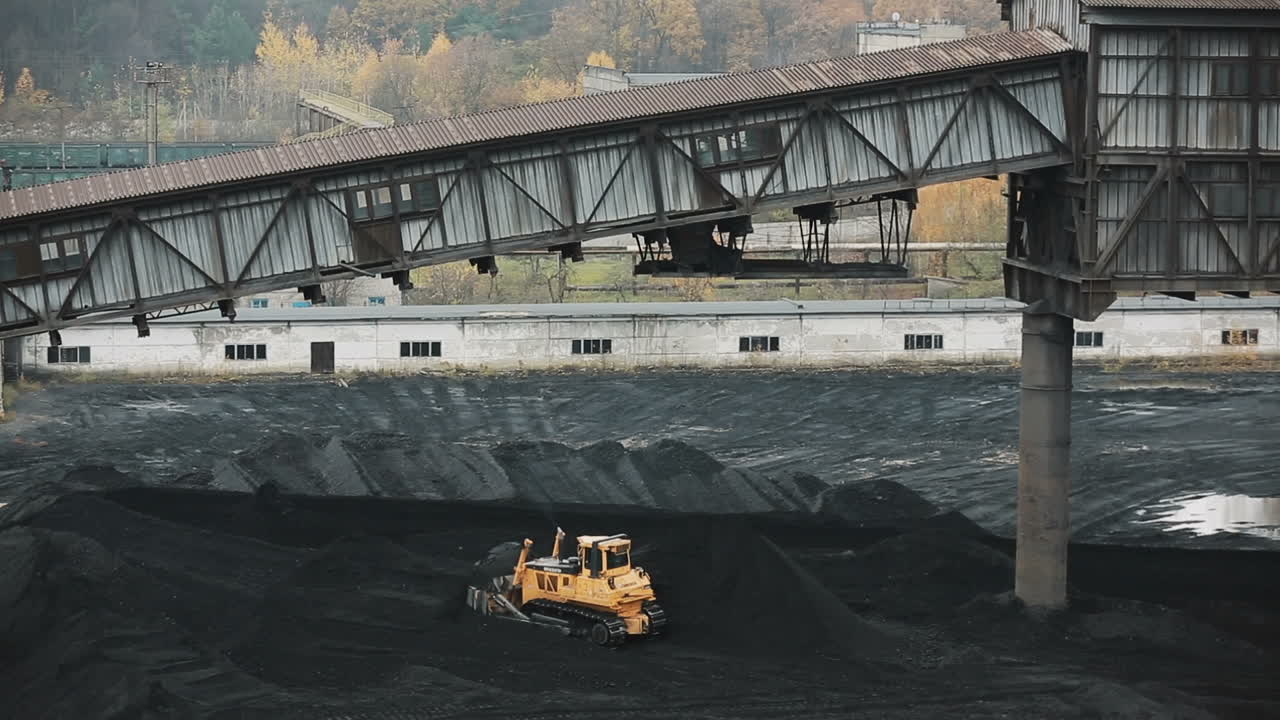 Warehouse of coal inventory plant. Yellow tractor loading the coal on ...