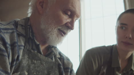 elderly man teaching young student how to use pottery wheel