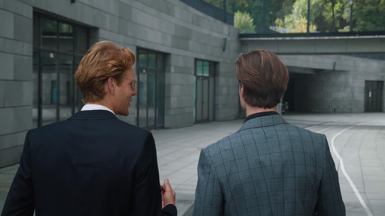 la vista posteriore di due uomini d'affari colleghi in abiti formali che chiacchierano sulla strada per il lavoro. due uomini dipendenti manager che parlano mentre camminano in centro.