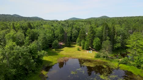 drone-shot-of-Adirondack-camp-with-canoes-resting-on-the-shore-with-mountains-in-the-background