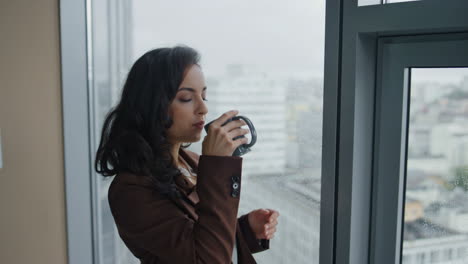 businesswoman drinking coffee standing near office panoramic window close up.