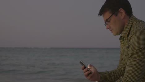 young man using smart phone by sea in the evening