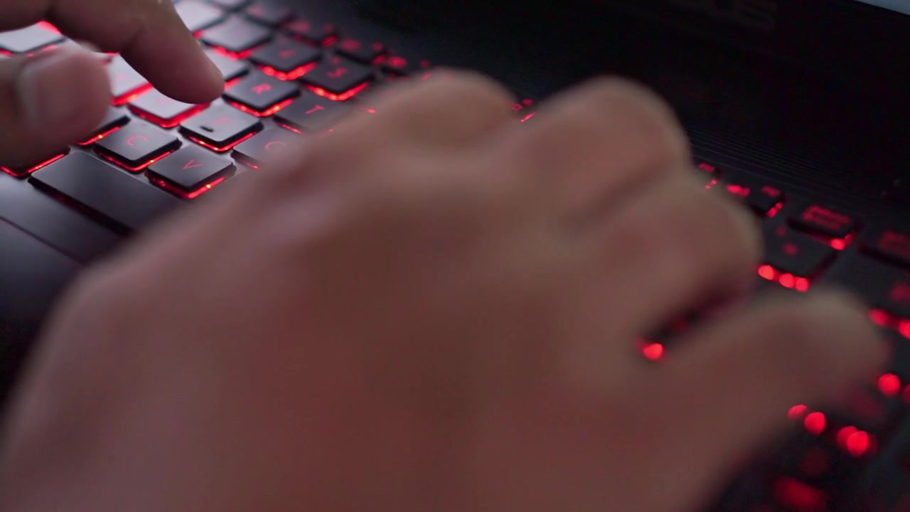 Tangan seseorang mengetik di keyboard laptop dengan lampu LED merah, pekerjaan digital, dan gaya hidup teknologi