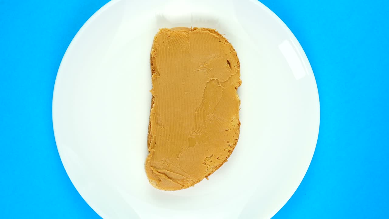 TOP VIEW: Plate with peanut butter sandwich rotates on a blue background